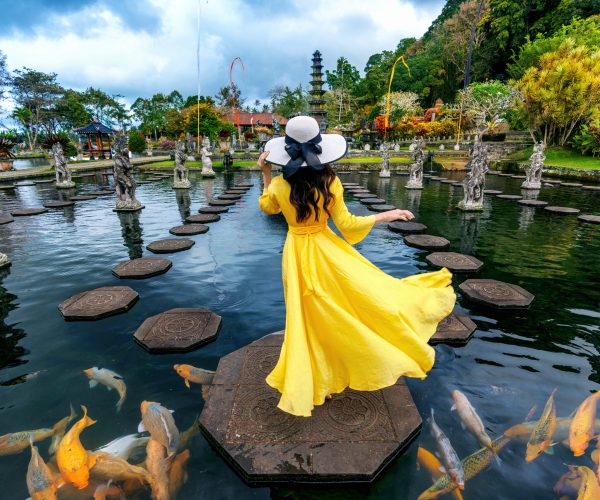 Woman standing in pond with colorful fish at Tirta Gangga Water Palace in Bali, Indonesia.